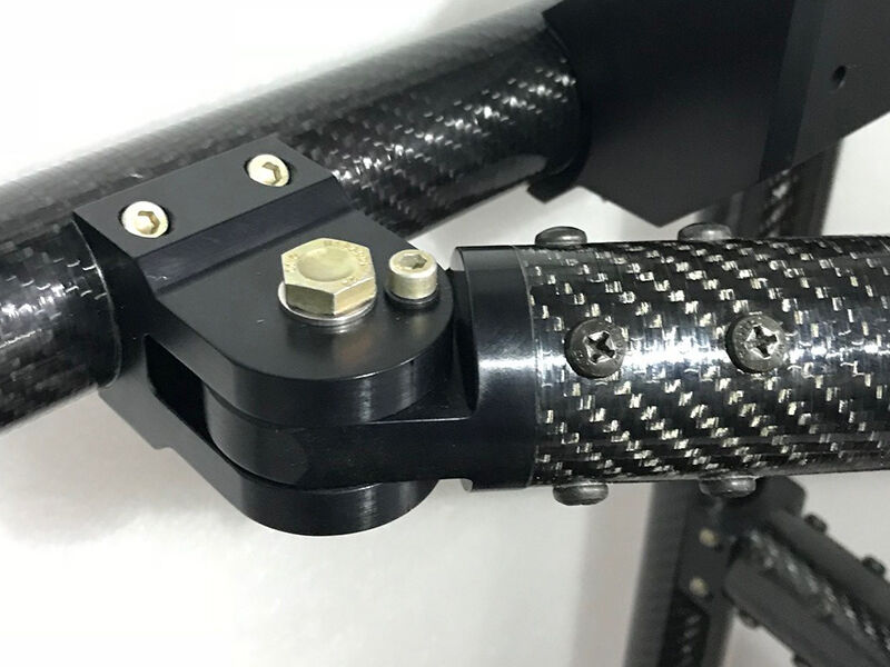 Image shows a dark angular structure on a white ground. It highlights the CARBONNect™ adjustable joint section of the monitor arm with integrated carbon fiber tubing on the avionics workstation. The black metallic joiner is connected to side of a tube and the adjustable section of that joiner attaches to the end of a different carbon tube..